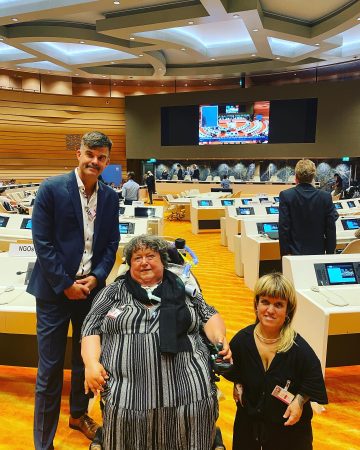 Gruppenbild von Buchner, Feuerstein und Rammel mit Blick in den Saal hinein der halbrund angelegt ist mit großem Screen