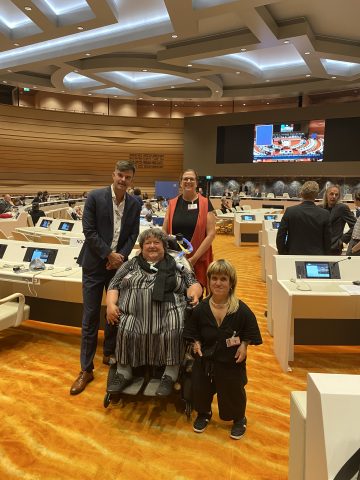 Gruppenbild von Buchner, Egger, Feuerstein und Rammel mit Blick in den Saal hinein der halbrund angelegt ist mit großem Screen