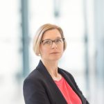 Frau mit kinnlangen blonden Haaren und Brille in Blazer