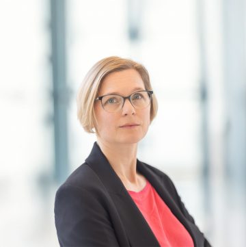 Frau mit kinnlangen blonden Haaren und Brille in Blazer