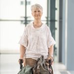 ältere Frau mit weißen Haaren und weißer Bluse schaut mit Rollator in die Kamera