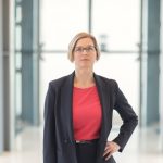Frau mit kinnlangen blonden Haaren und Brille in Blazer mit Hand in der Hüfte