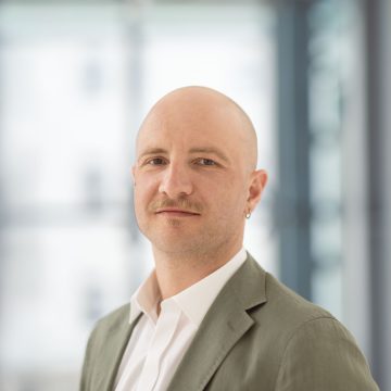 junger Mann mit Oberlippenbartl, Ohrring und grauem Anzug