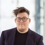 Person mit kurzen Haaren, Brille, Bart und dunklem Blazer