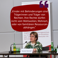 Kleinwüchsige Frau mit Vokuhila und grüner Jacke spricht auf Podium mit Zitat: „Kinder mit Behinderungen sind Trägerinnen und Träger von Rechten. Ihre Rechte dürfen nicht vom Wohlwollen, Wohnort, oder von familiären Ressourcen abhängen.“ Daniela Rammel